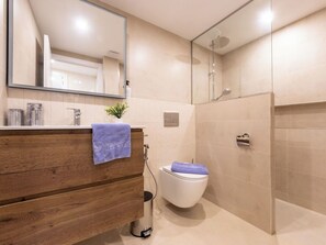 Uma casa de banho moderna com toucador de madeira, sanita, chuveiro e espelho.