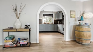Eine moderne Küche mit grauen Schränken, einem Holzfass und Blick durch einen Bogen in einen Essbereich.