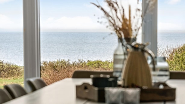 Ein Tisch mit einer Vase mit getrockneten Pflanzen und einer Kerze, mit Blick auf ein ruhiges Meer.
