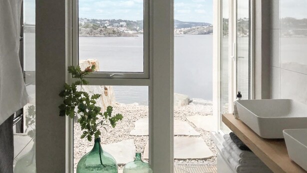 A bathroom with a large window overlooking a body of water and a distant town. - Stunning home in Stabbestad (Stabbestad)