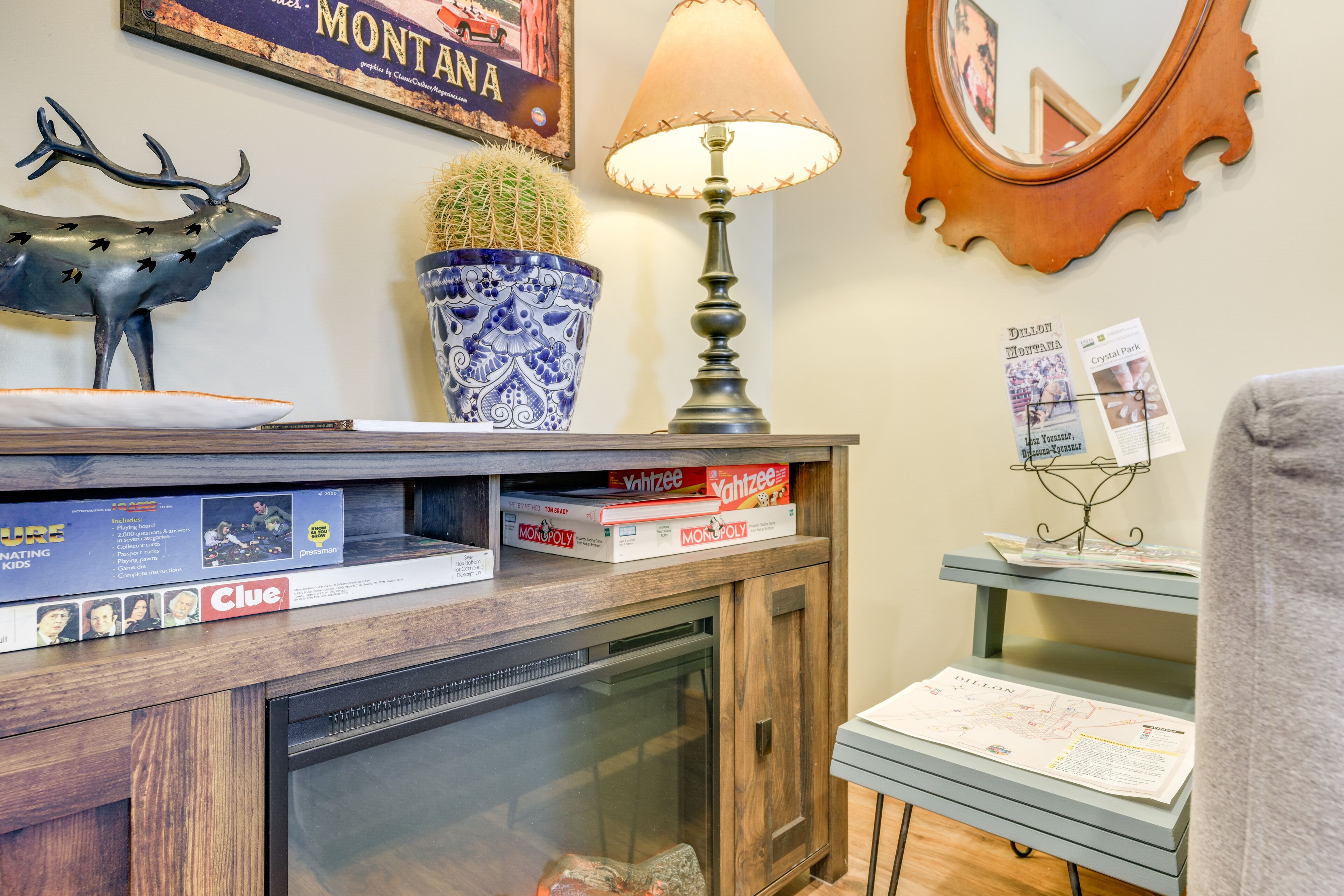 A wooden cabinet with a glass door, a lamp, a cactus, a deer sculpture, and a framed picture of Montana.