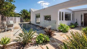 A modern house with a swimming pool, surrounded by tropical plants and a thatched fence. - Pet Friendly - Skomer House Portsea with gas heated pool. Steps to beach and Portsea Pub (Portsea)