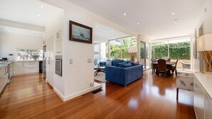 A spacious kitchen with modern appliances, a dining area with a blue sofa, and large windows offering a view of greenery. - Pet Friendly - Skomer House Portsea with gas heated pool. Steps to beach and Portsea Pub (Portsea)