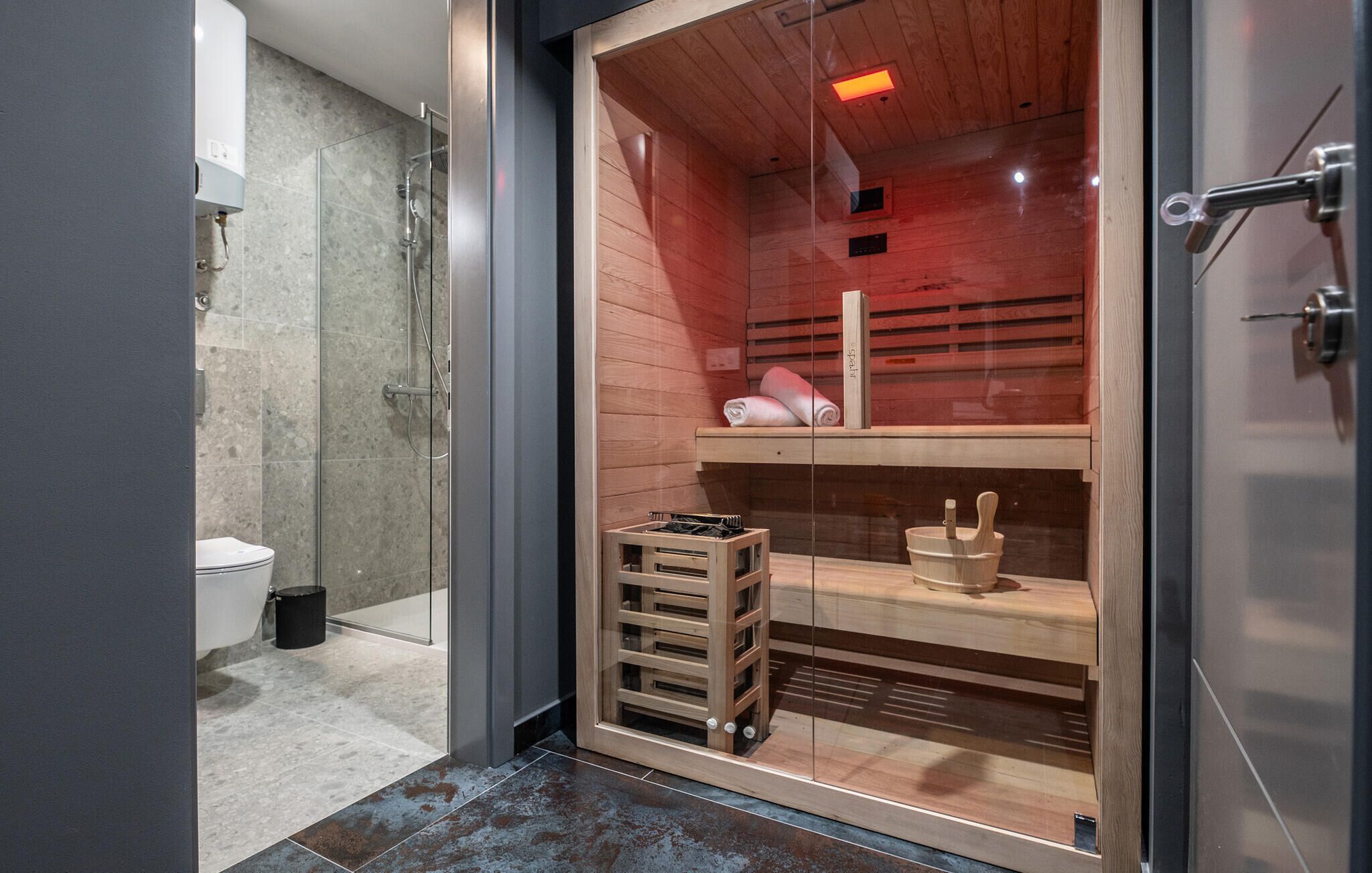 Ein modernes Badezimmer mit Glasabtrennung, einer sichtbaren Duschfläche und einem Holzboden mit Handtüchern.