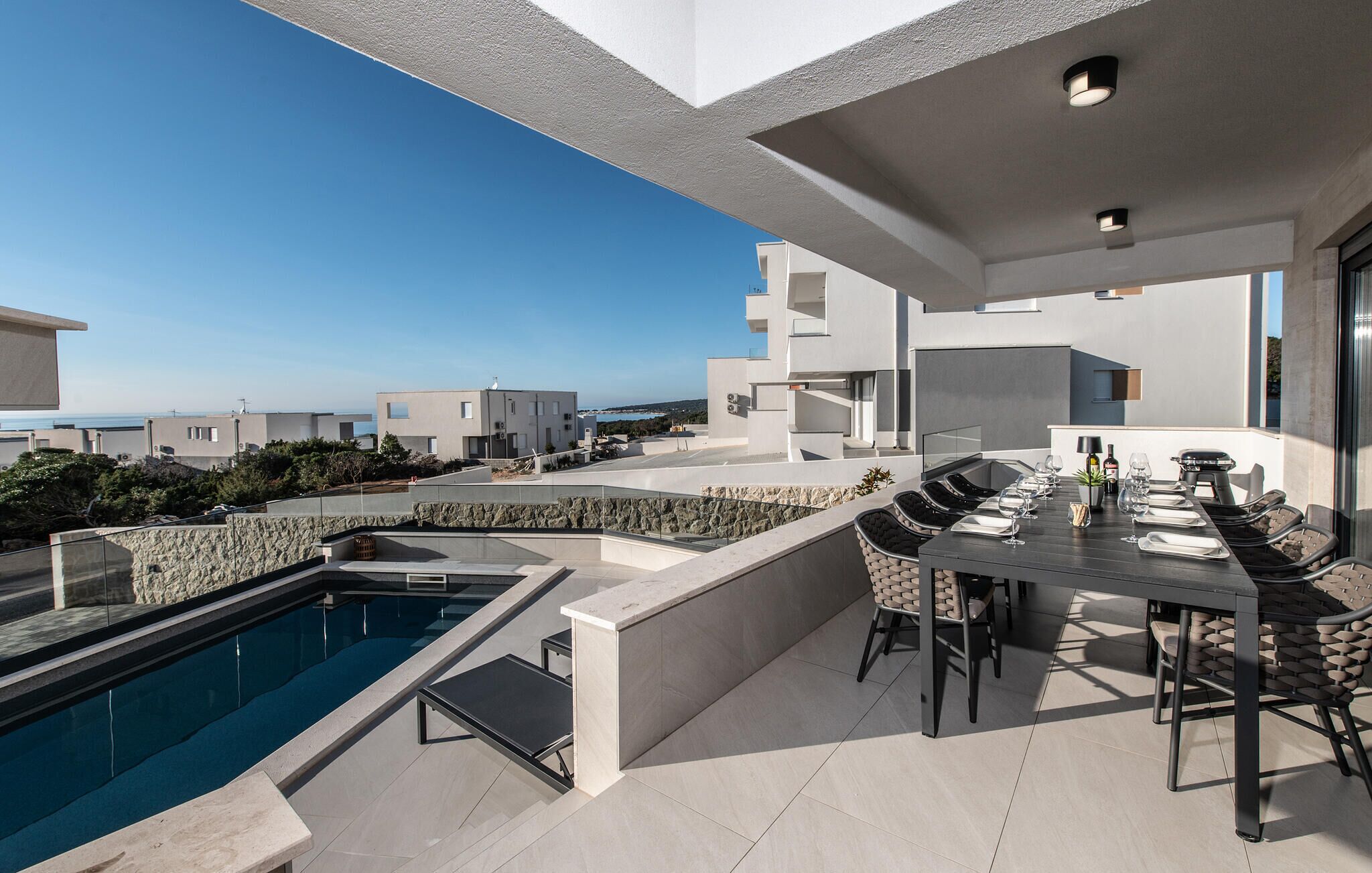 Ein moderner Essbereich im Freien mit Pool, Steinmauern und freiem Blick auf das Meer.