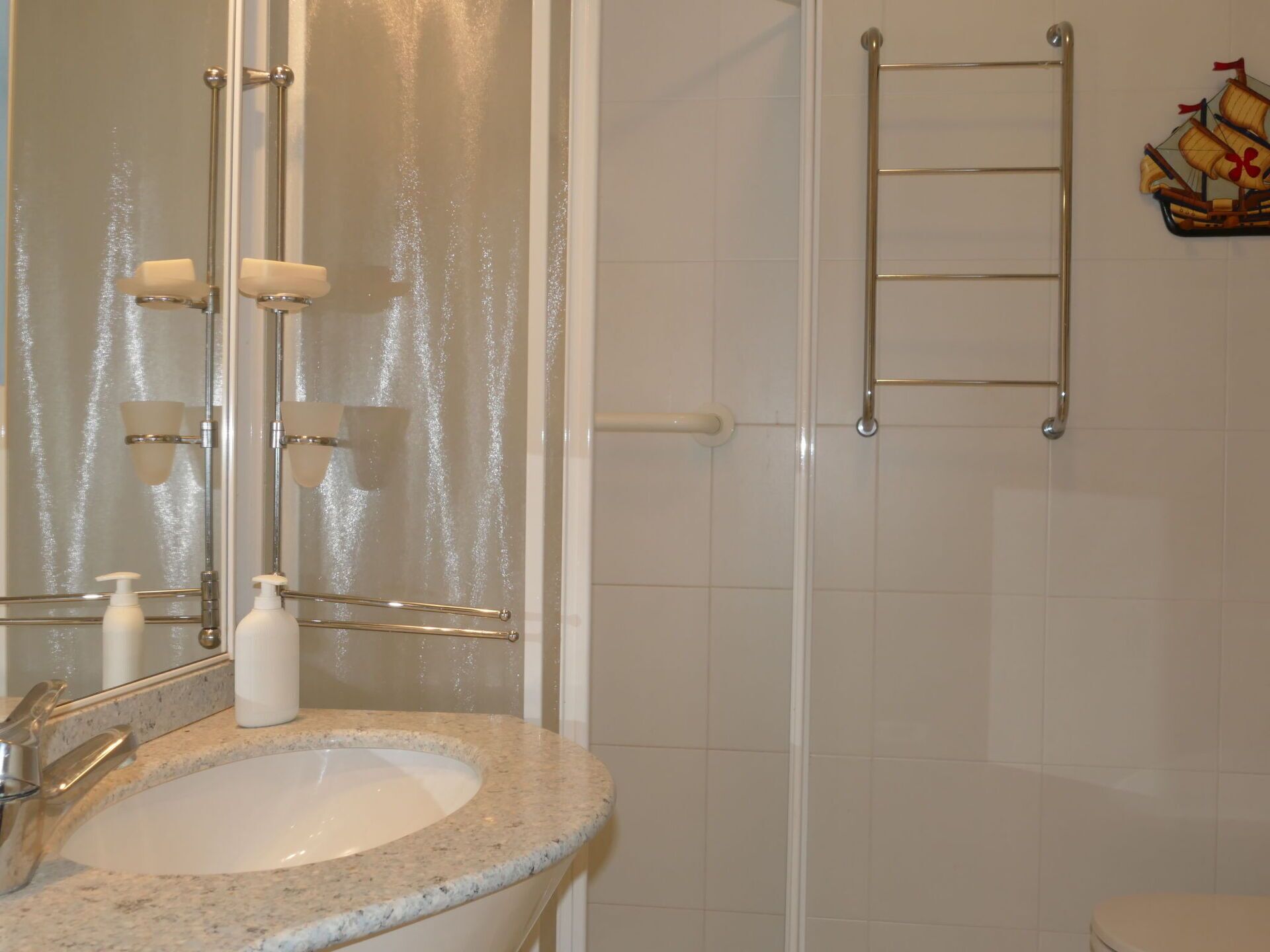 A bathroom with a granite sink, a mirror, a towel rack, and a shower area.
