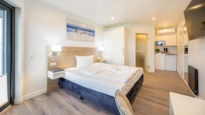 Una habitación de hotel moderna con una cama grande, mesitas de noche, un escritorio y una kitchenette.