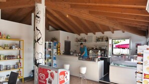 A café with a wooden ceiling, a counter with a person serving, shelves with snacks, and a display of pastries.