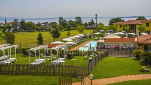 A pool area with lounge chairs and umbrellas, surrounded by a wooden fence and a view of a lake.