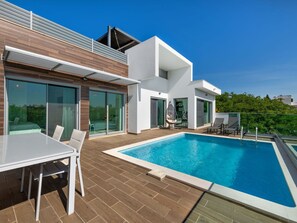 Una casa moderna con piscina, zona pranzo e una sedia a dondolo.