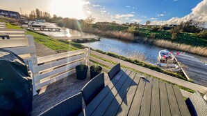 A riverside deck with seating, a boat docked, and a building in the background.