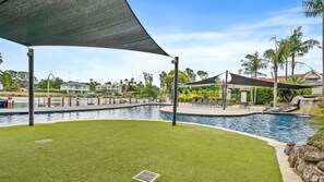 Una piscina con un área verde circundante, sillas de descanso y una fuente de agua.