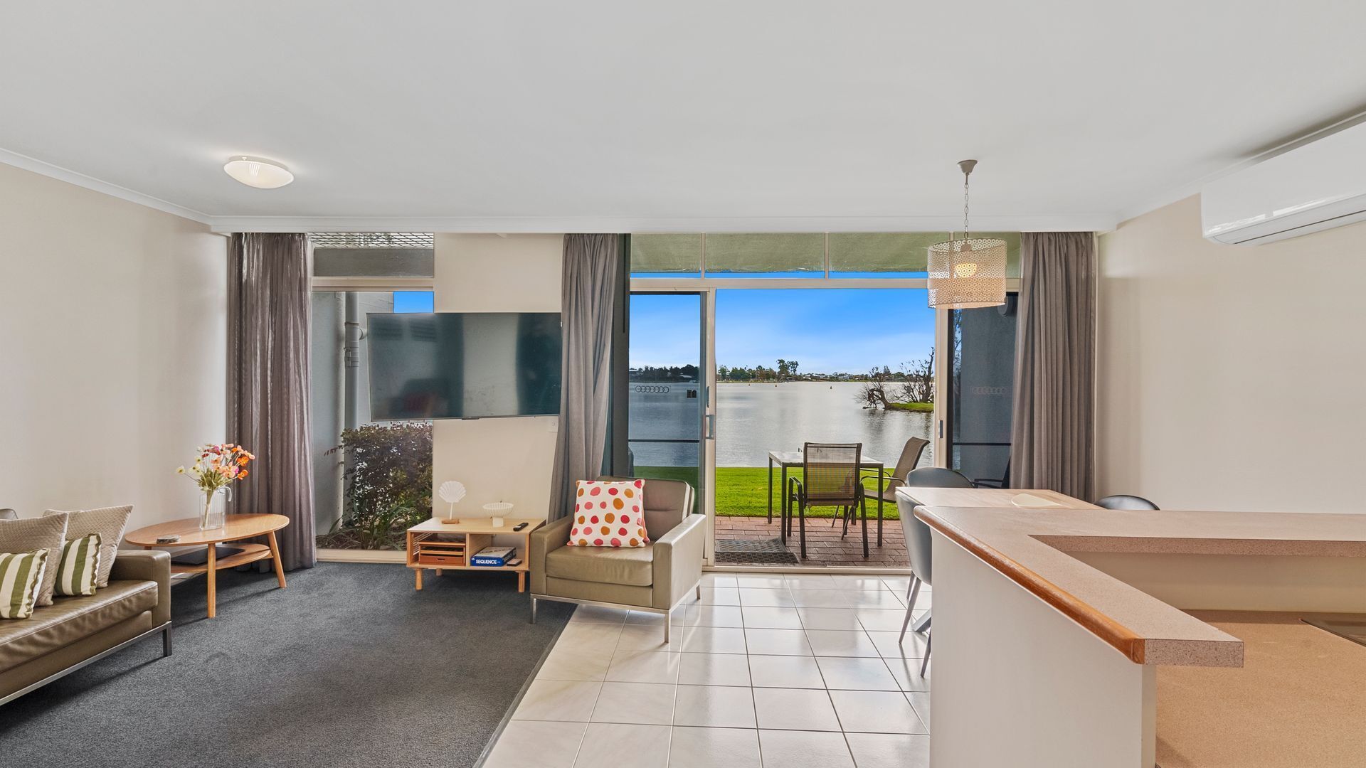 A modern living room with a sofa, a small table, and a chair. There is a balcony with a view of a lake.