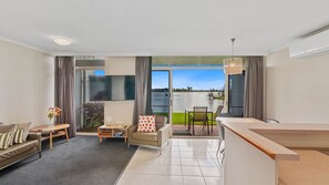Ein modernes Wohnzimmer mit einer Couch, einem kleinen Tisch und einem Sessel. Ein Balkon bietet Blick auf einen See.