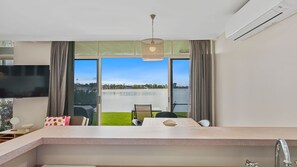 Una habitación de hotel moderna con un ventanal grande, un televisor de pantalla plana, una zona de comedor con mesa y sillas, y una lámpara colgante.