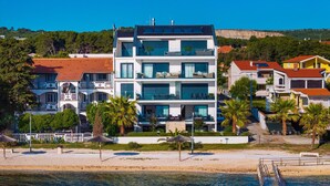 A multi-story building with balconies, a beach in the foreground, and a cliff in the background.
