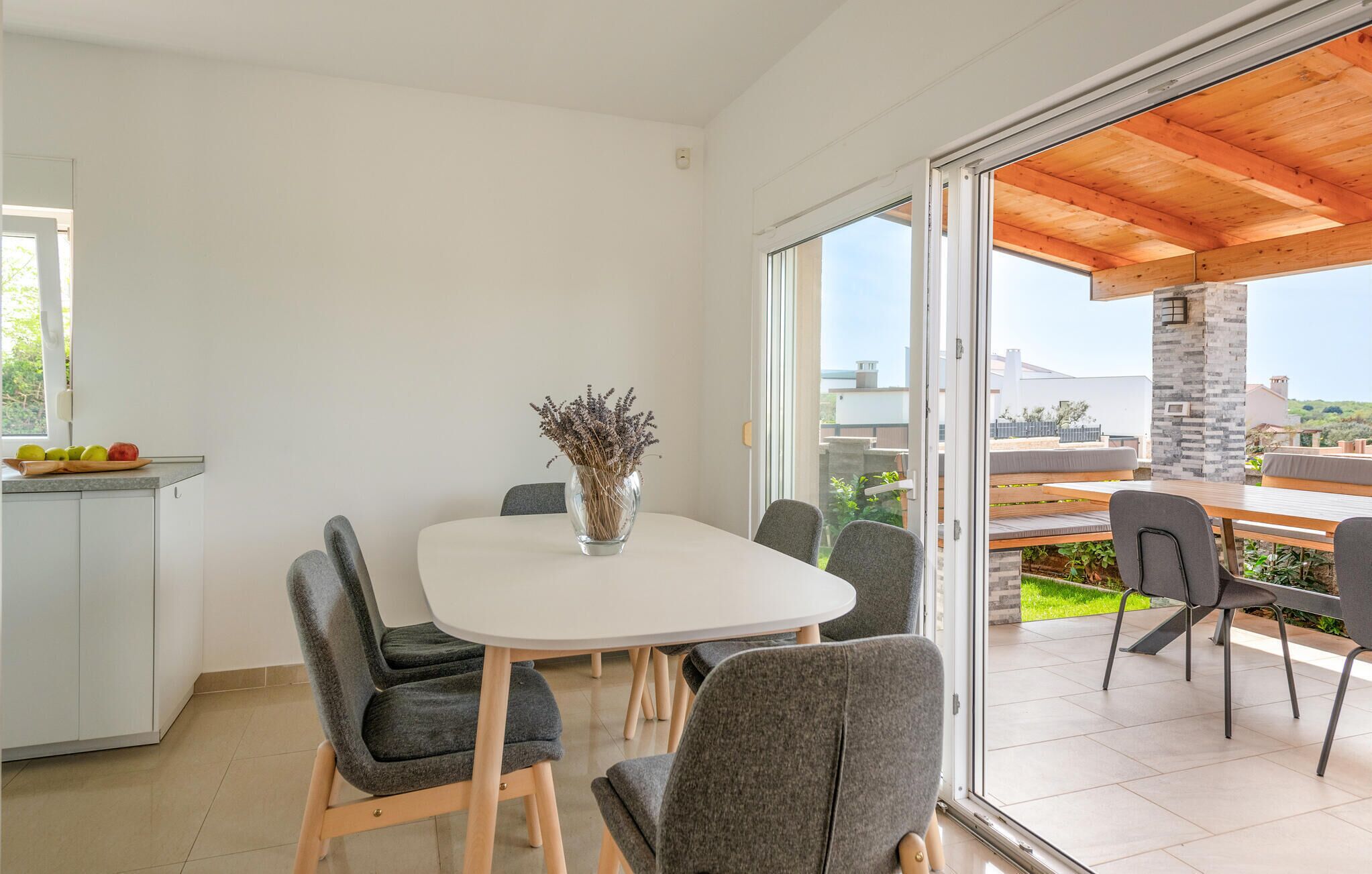 A modern kitchen with a dining area, large windows, and a view of the outdoors.