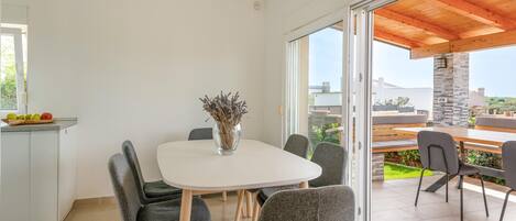 A modern kitchen with a dining area, large windows, and a view of the outdoors.