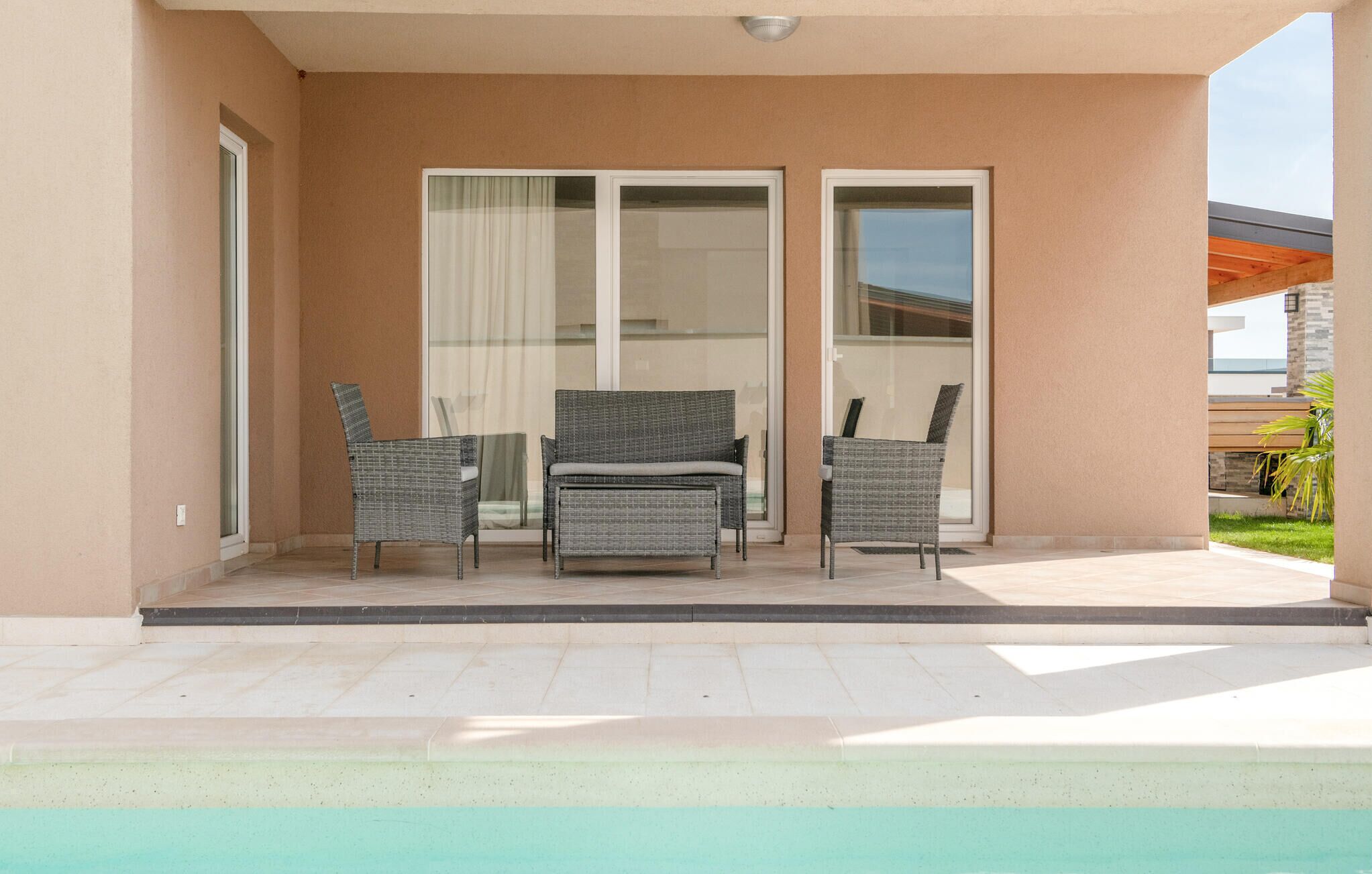 A covered patio with a pool, featuring a sliding glass door, two wicker chairs, and a bench.