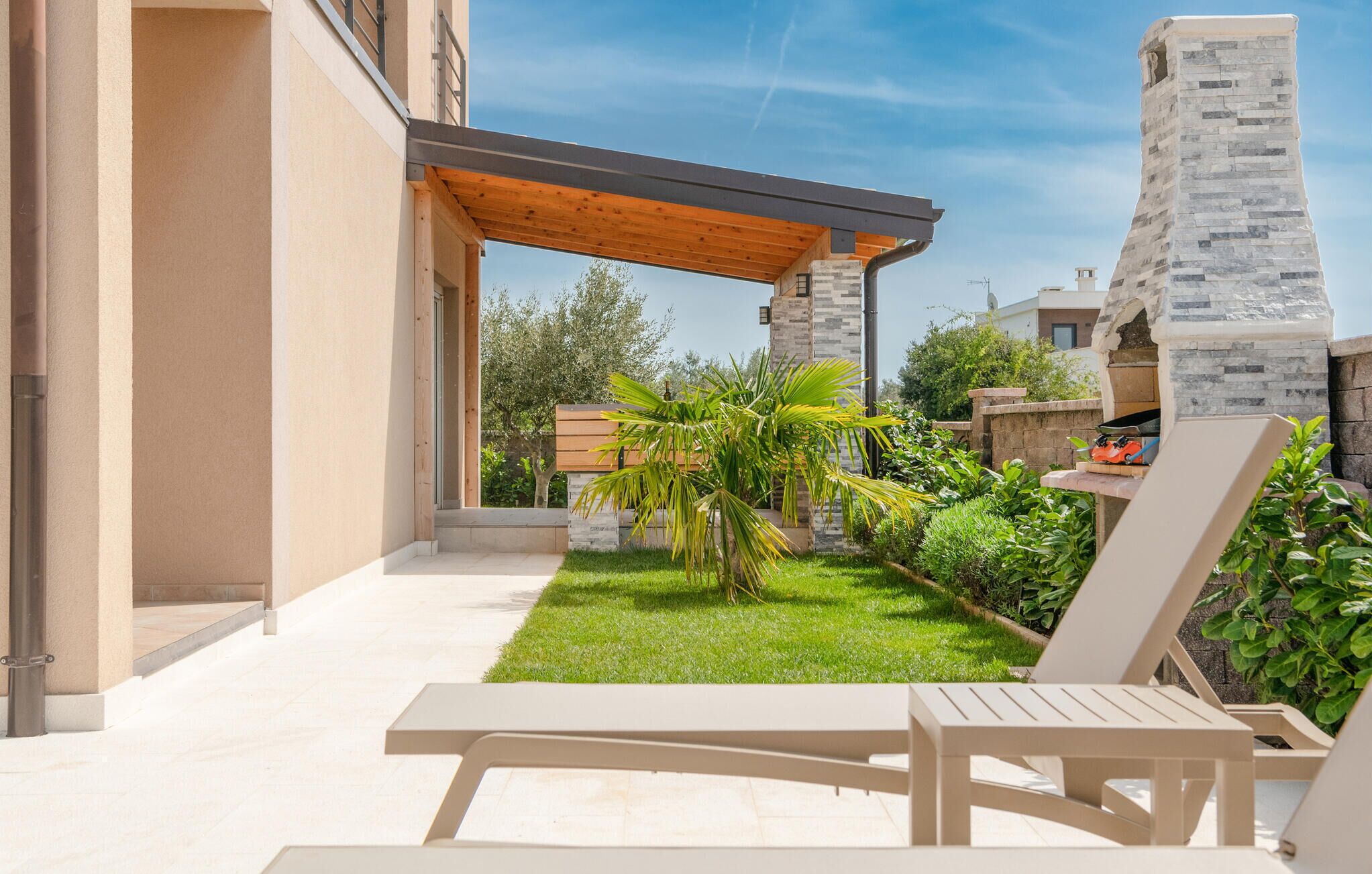 Eine Terrasse mit einer Pergola, einem Steinofen und einem kleinen Garten mit Palmen.