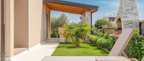 Eine Terrasse mit einer Pergola, einem Steinofen und einem kleinen Garten mit Palmen.