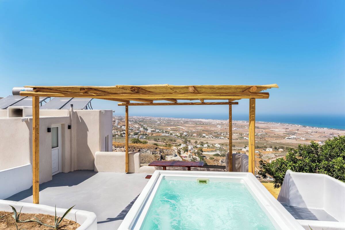 A rooftop terrace with a wooden pergola, a hot tub, and a view of the coastline.