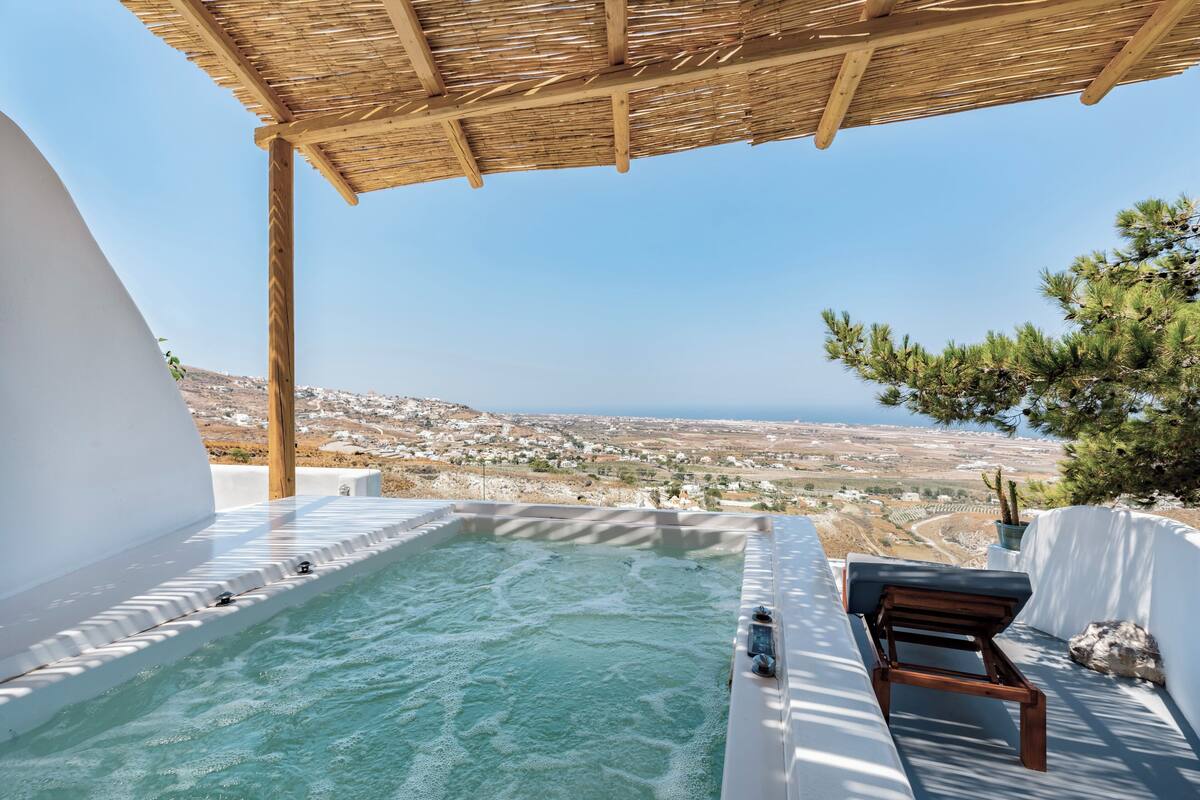A hot tub with a wooden bench, a pergola overhead, and a view of a coastal landscape.