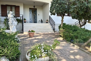 A stone staircase leading to a door, surrounded by potted plants and a statue.