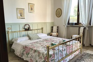 A bed with a floral bedspread, a wooden headboard, and a window with curtains.