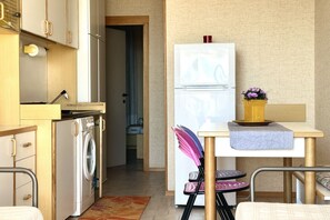 Cozinha compacta com máquina de lavar, geladeira e área de refeições com mesa e cadeiras.