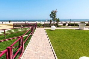 A paved walkway with a red railing, a grassy area, and a view of the sea.