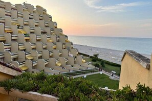 A modern hotel with a unique geometric facade, a beachfront view, and a well-maintained lawn.