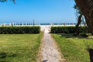 Uma trilha pavimentada conduz a uma praia com cercas brancas e uma vista desobstruída do oceano.