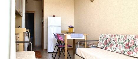 A compact room with a bed, a small kitchenette, a dining table, and a chair.