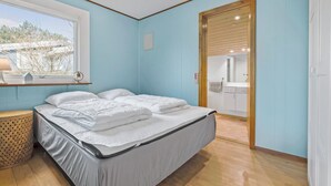 Ein Schlafzimmer mit Bett, Fenster, Holztür und einem kleinen Nachttisch.