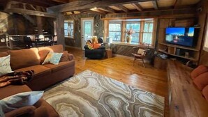 L’intérieur chaleureux d’un chalet avec un plancher en bois, un canapé, un téléviseur et une cheminée.