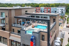 A modern building with a rooftop pool area, multiple balconies, and a brick facade.
