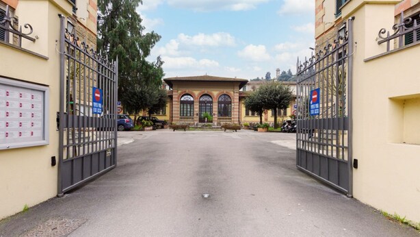 Entrada fechada por portão com um edifício ao fundo, área de estacionamento e placa de proibido a entrada.