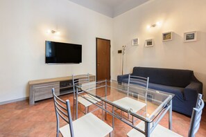 A modern living room with a glass-top table, chairs, a flat-screen TV, a sofa, and a door.