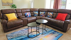 A brown leather sectional sofa with colorful cushions, two small black tables, and a large abstract rug. - Beautiful Paradise Park Hale (Keaau)