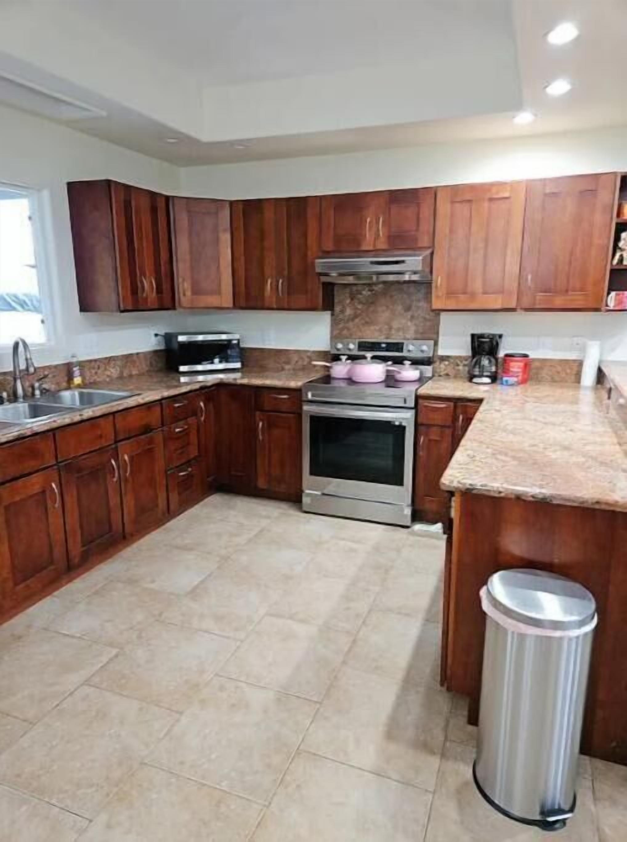 A kitchen with wooden cabinets, a stainless steel oven, a coffee maker, and a trash can.