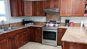 A kitchen with wooden cabinets, a stainless steel oven, a coffee maker, and a trash can. - Beautiful Paradise Park Hale (Keaau)