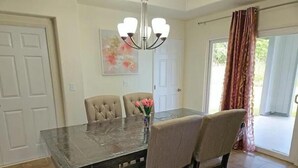 A dining room with a dark wooden table, beige upholstered chairs, a chandelier, and a painting on the wall. - Beautiful Paradise Park Hale (Keaau)