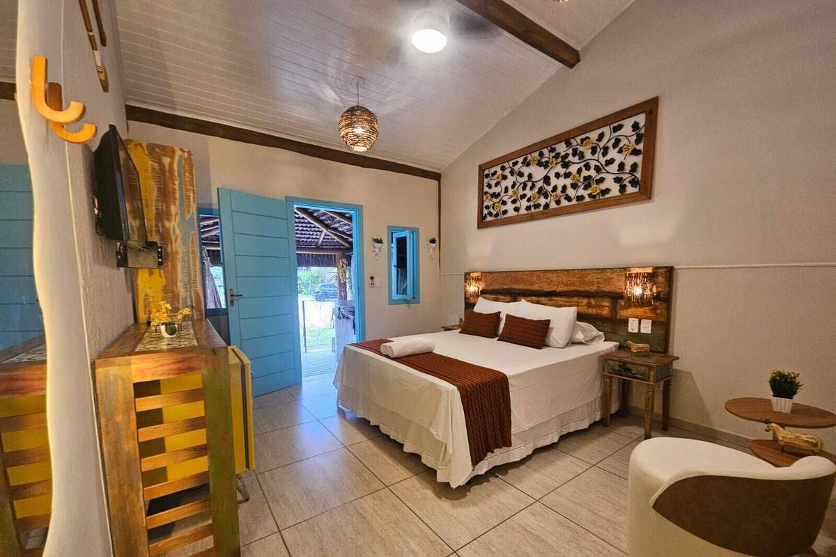 A bedroom with a bed, bedside tables, a chair, a decorative wall piece, and a door leading to an outdoor area.