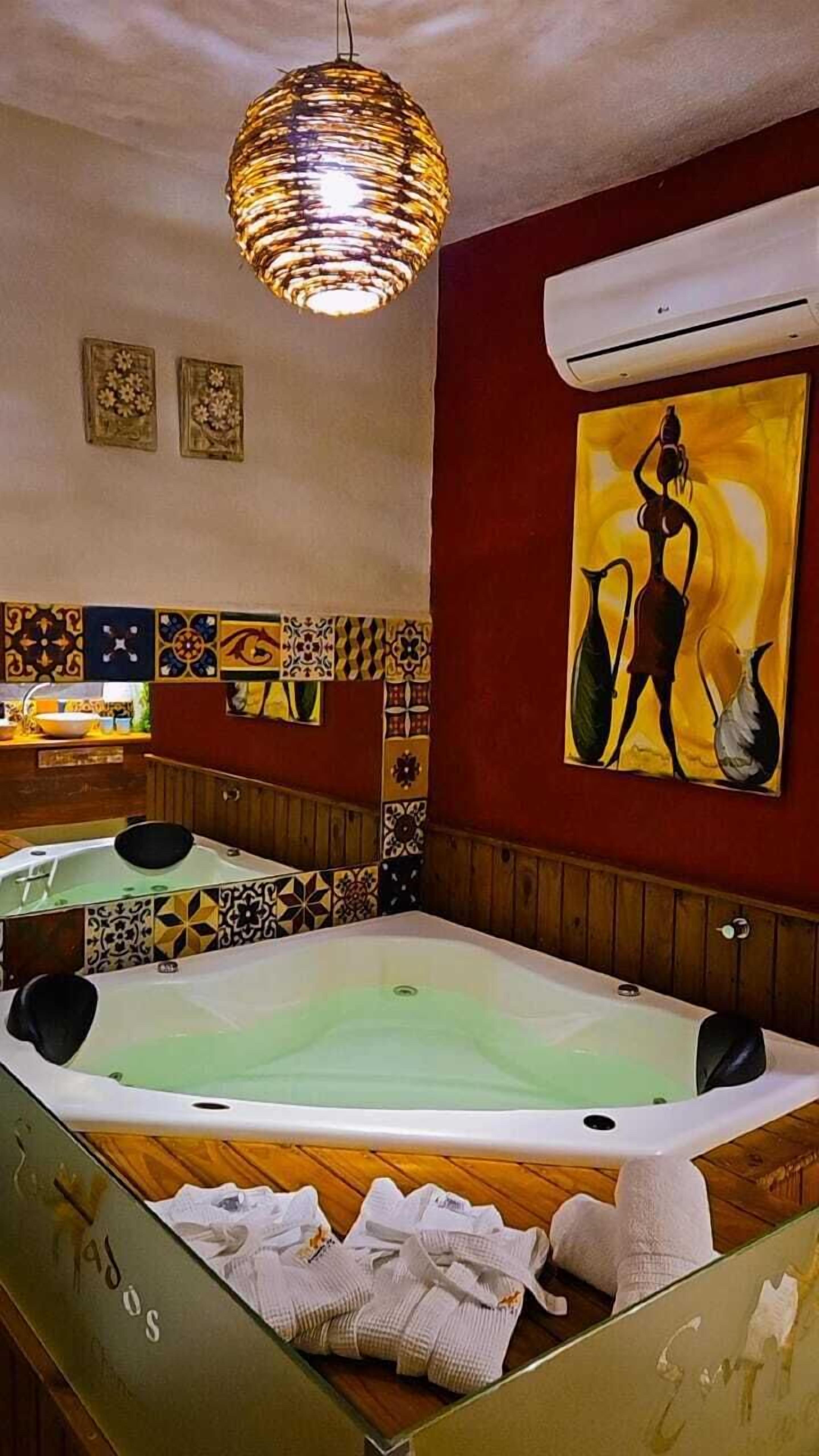 A spa room with two hot tubs, a decorative wall with a painting, and a ceiling light fixture.