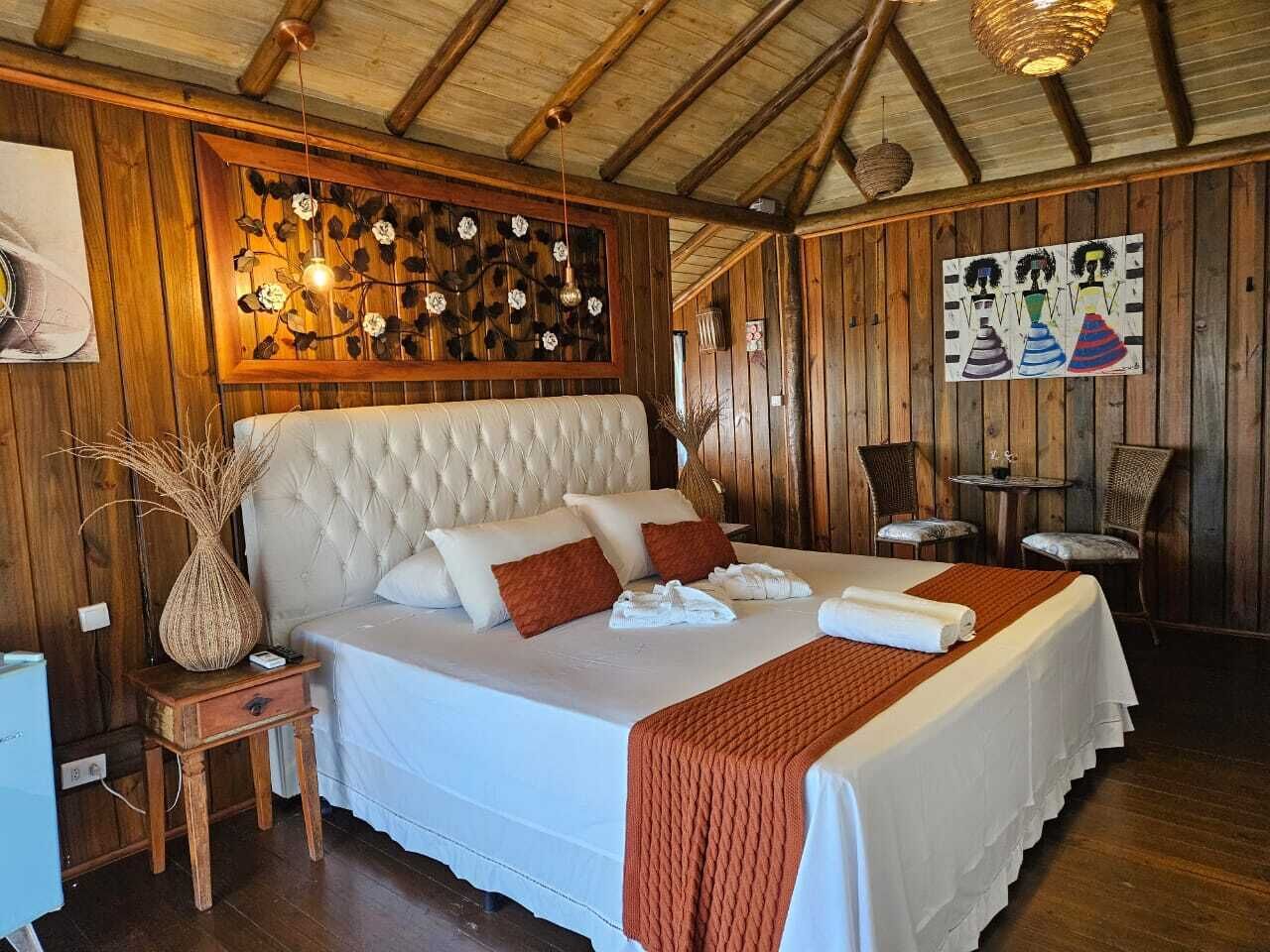 Un dormitorio con una cama grande, paredes de madera, un adorno en la pared y una mesita con un jarrón.