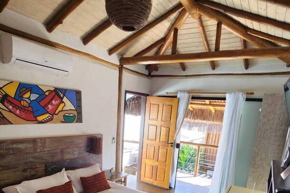 A spacious bedroom with a large bed, wooden beams, a hanging light fixture, and a view of the outdoors.