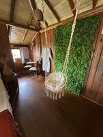Un interior rústico de madera con una mecedora, una pequeña mesa redonda y una pared cubierta de follaje verde.