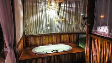 A wooden cabin with a wooden bathtub, a hanging light fixture, and sheer curtains.