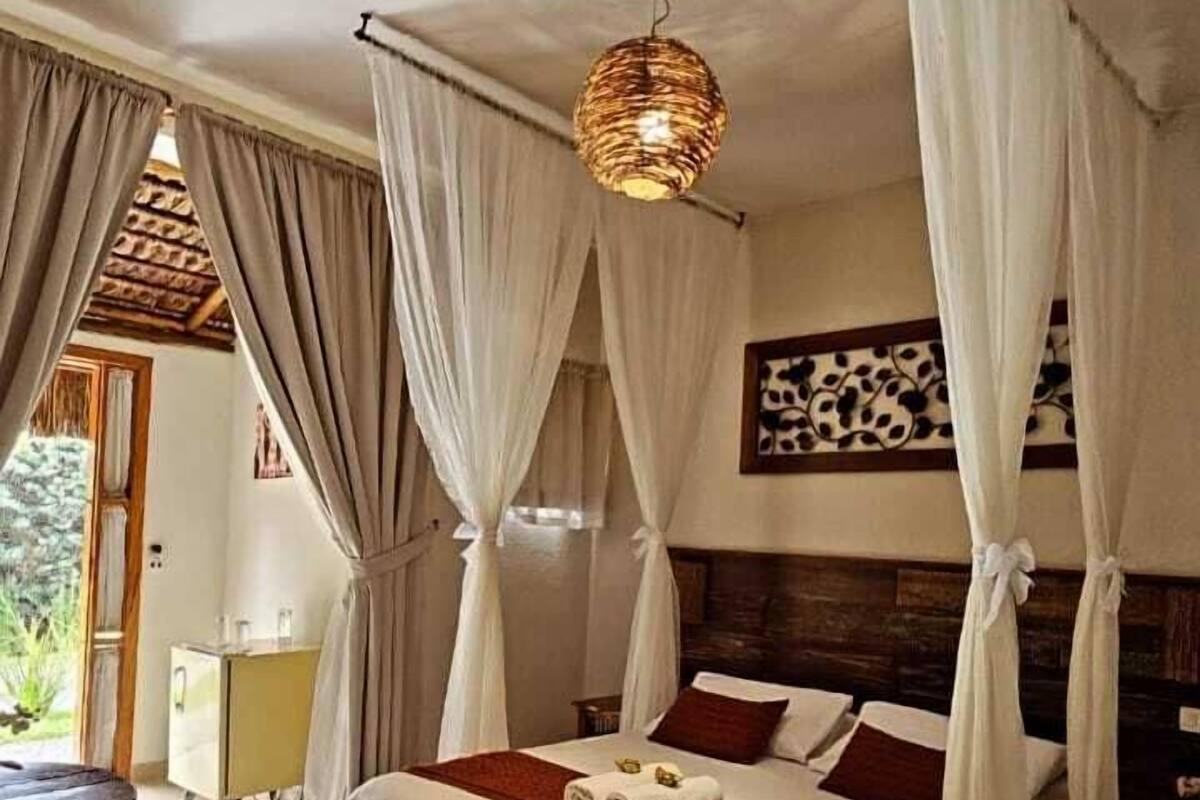 A bedroom with a bed, curtains, a hanging light fixture, and a wooden headboard.
